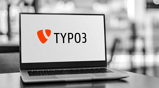 Laptop mit TYPO3-Logo auf dem Bildschirm, verschwommener Hintergrund.